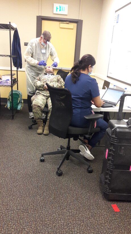 An unidentified Airman is receiving a dental exam as staff assistant records the notes and maintaining social distancing.