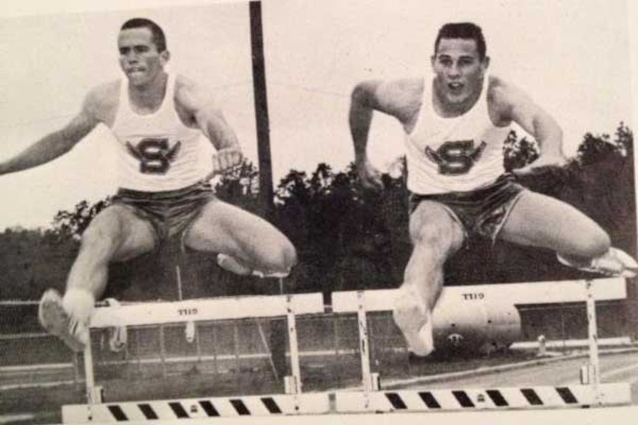 Two men jump hurdles on a track.