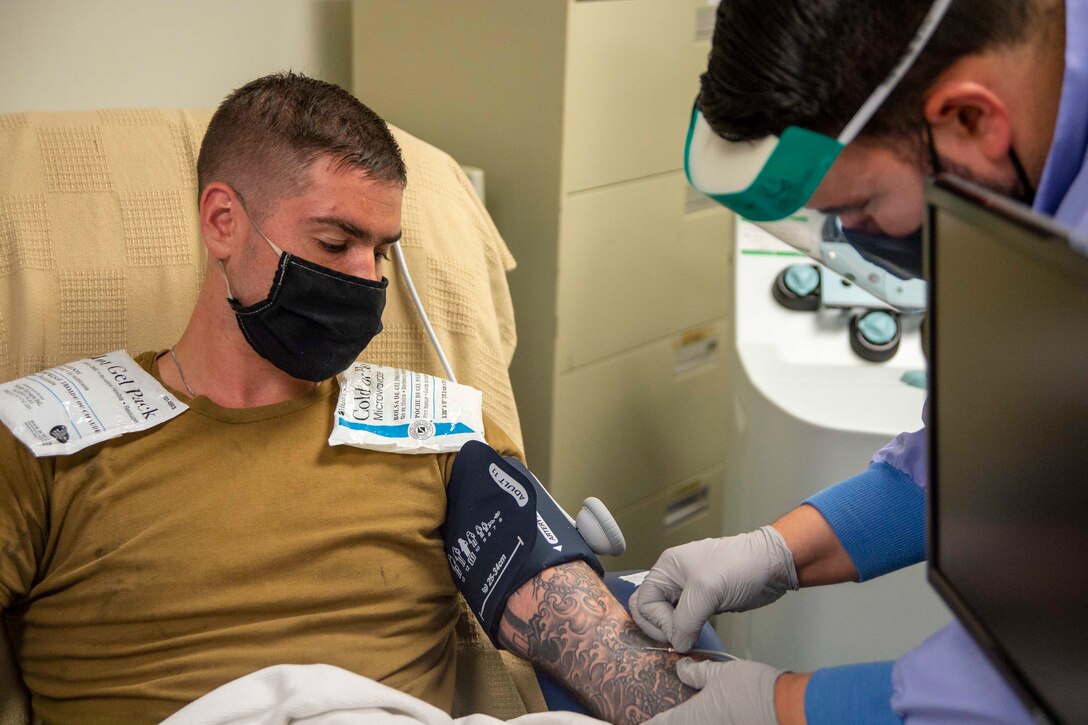 A phlebotomist wearing personal protective equipment collects a blood sample from a COVID-19 convalescent plasma donor.