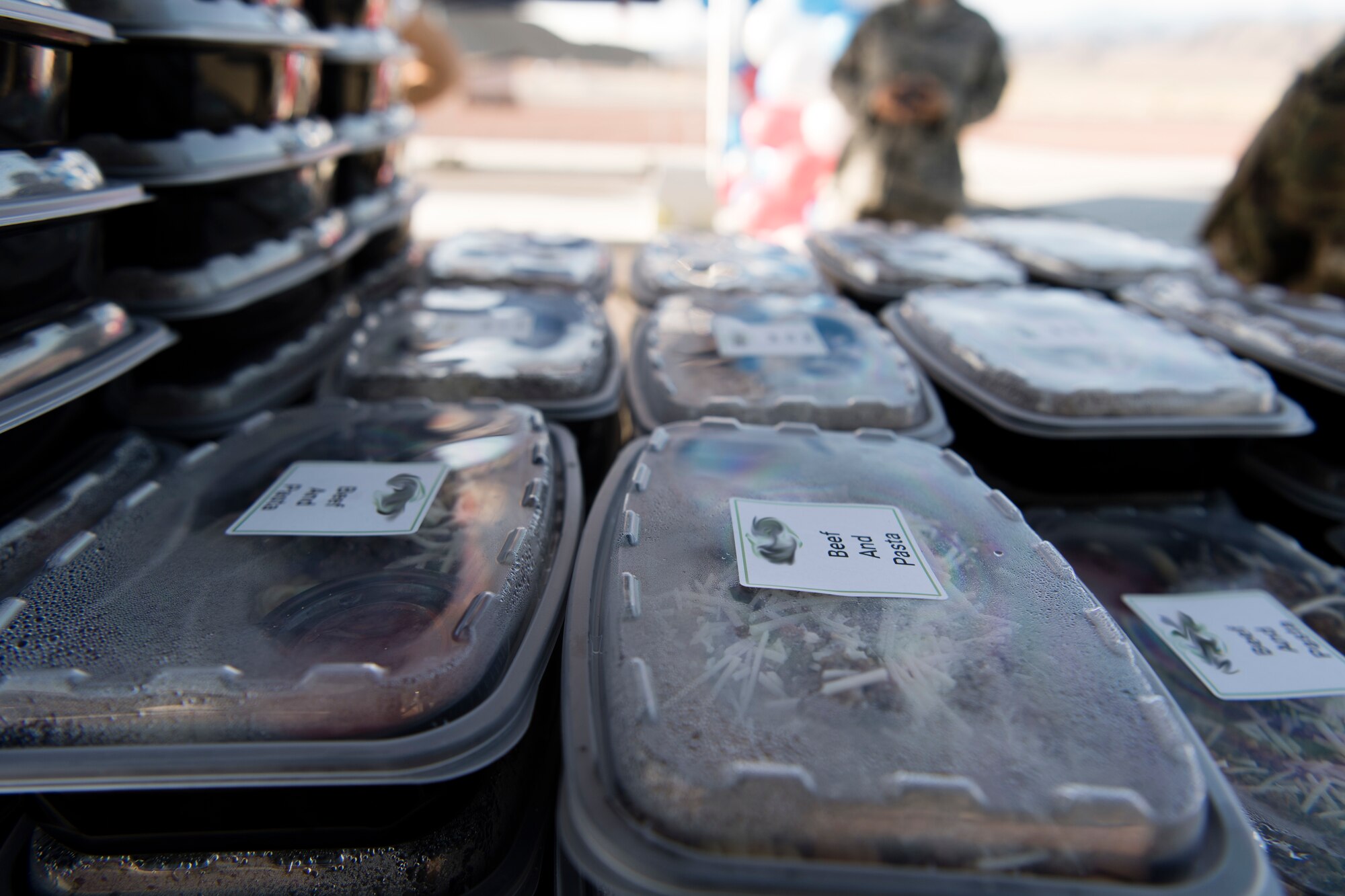 Stacks of the ready to eat meals rest on a table in the shade.