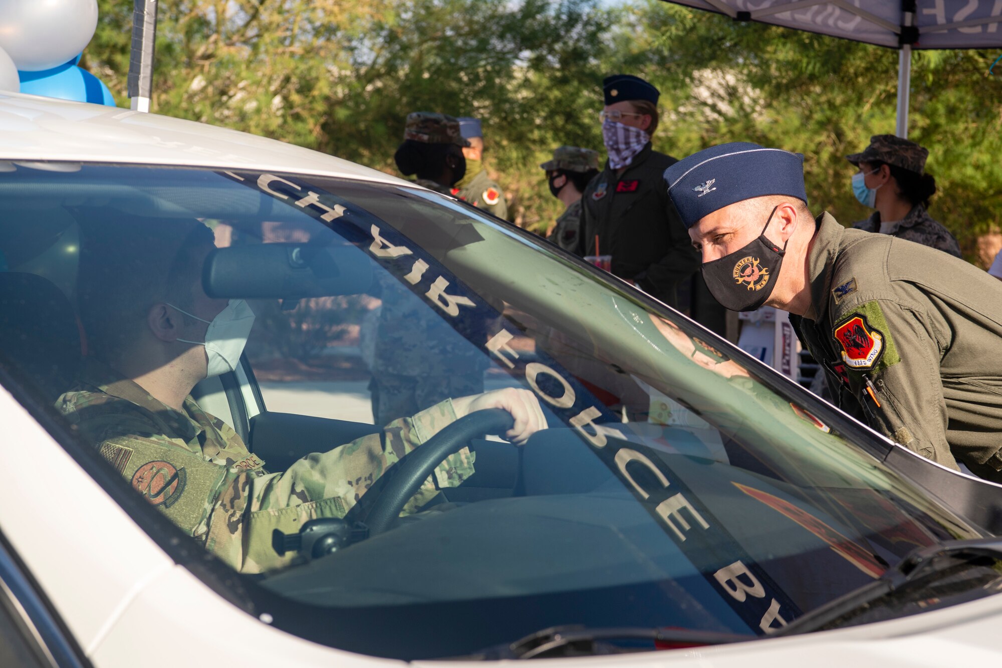 Col. Stephen Jones leans forward to speak to an Airmen in the divers seat of a white car durinig a morale event.
