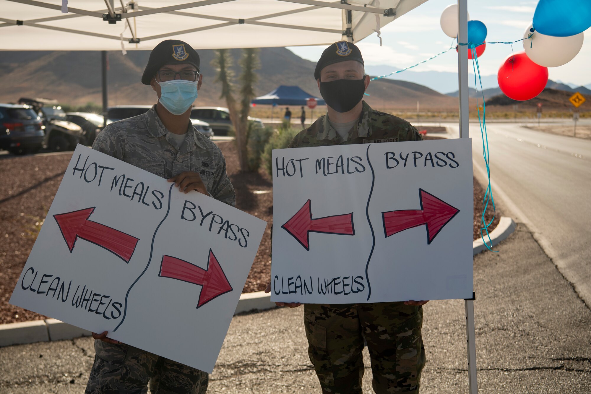 Two 432nd Security Forces Squadron hold signs with arrows that say "Hot meals & Clean Wheels" and Bypass.