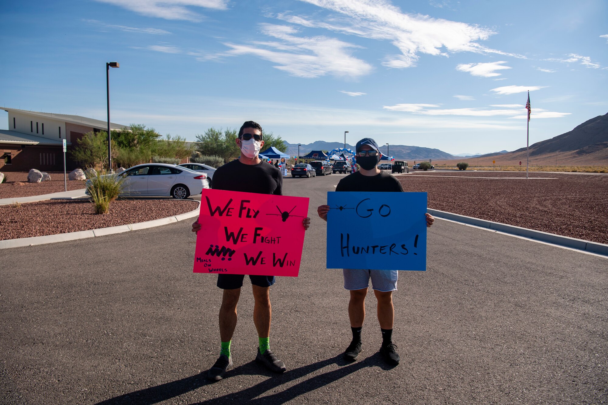 Two Airmen in civilian smile as one holds up a pink morale sign and the other a blue sign.