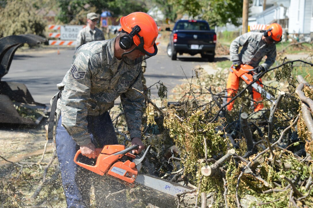 An airman uses a chainsaw to cut tree branches.