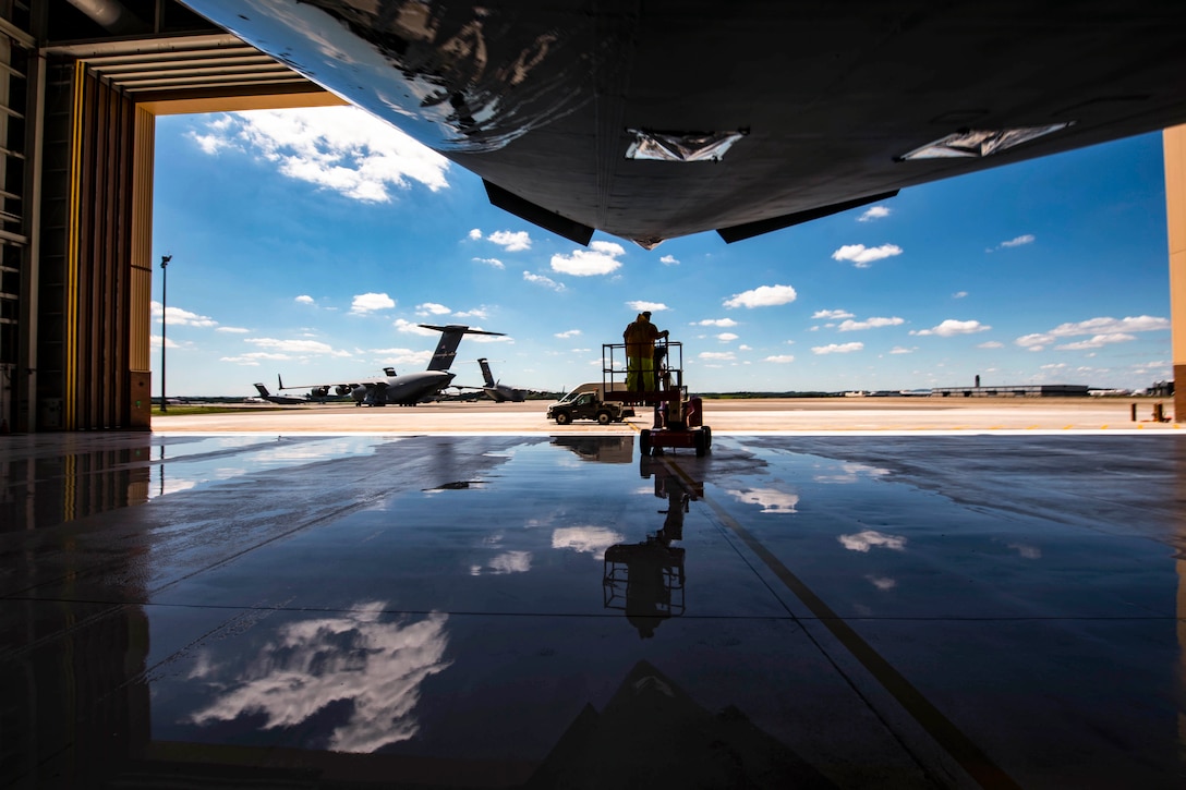 An airman rides towards an aircraft in a bay with other aircraft sitting in the background.