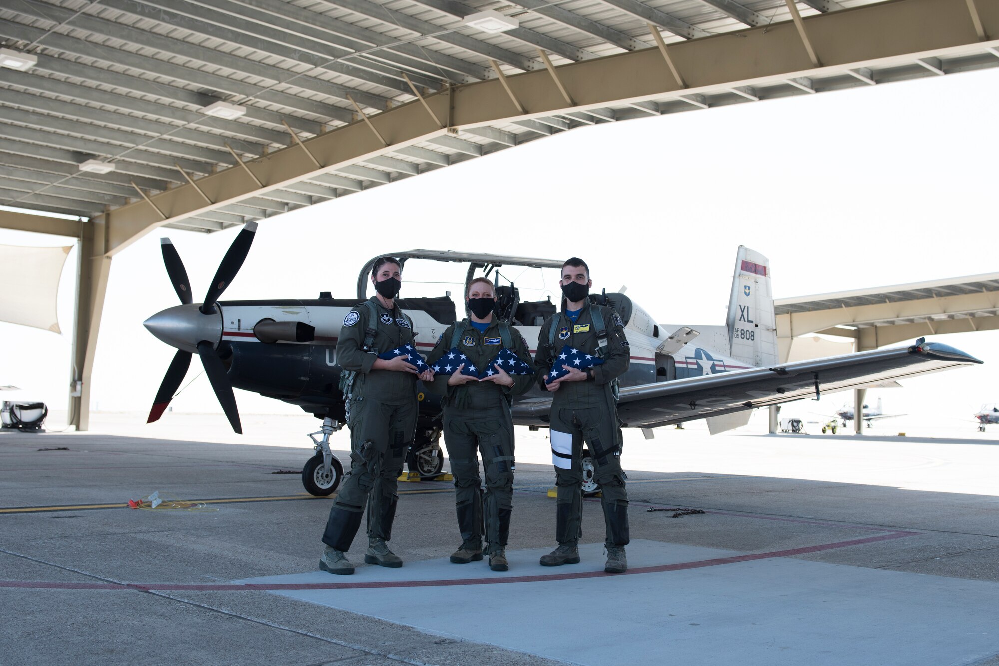 First Lt. April Wilcox, 85th Flying Training Squadron executive officer, Maj. Camber Governski, 96th FTS T-6A Texan II chief pilot, and 1st Lt. Will Friedman 85th FTS A-flight scheduler, pose in front of a T-6 on Aug. 14, 2020 at Laughlin Air Force Base, Texas, with the flags they are to fly for the families of the U.S. Customs and Border Protection service members who were lost to COVID-19. As they flew the flags, they practiced flying in formation to increase proficiency in order to train the student pilots more effectively. (U.S. Air Force photo by Senior Airman Anne McCready)