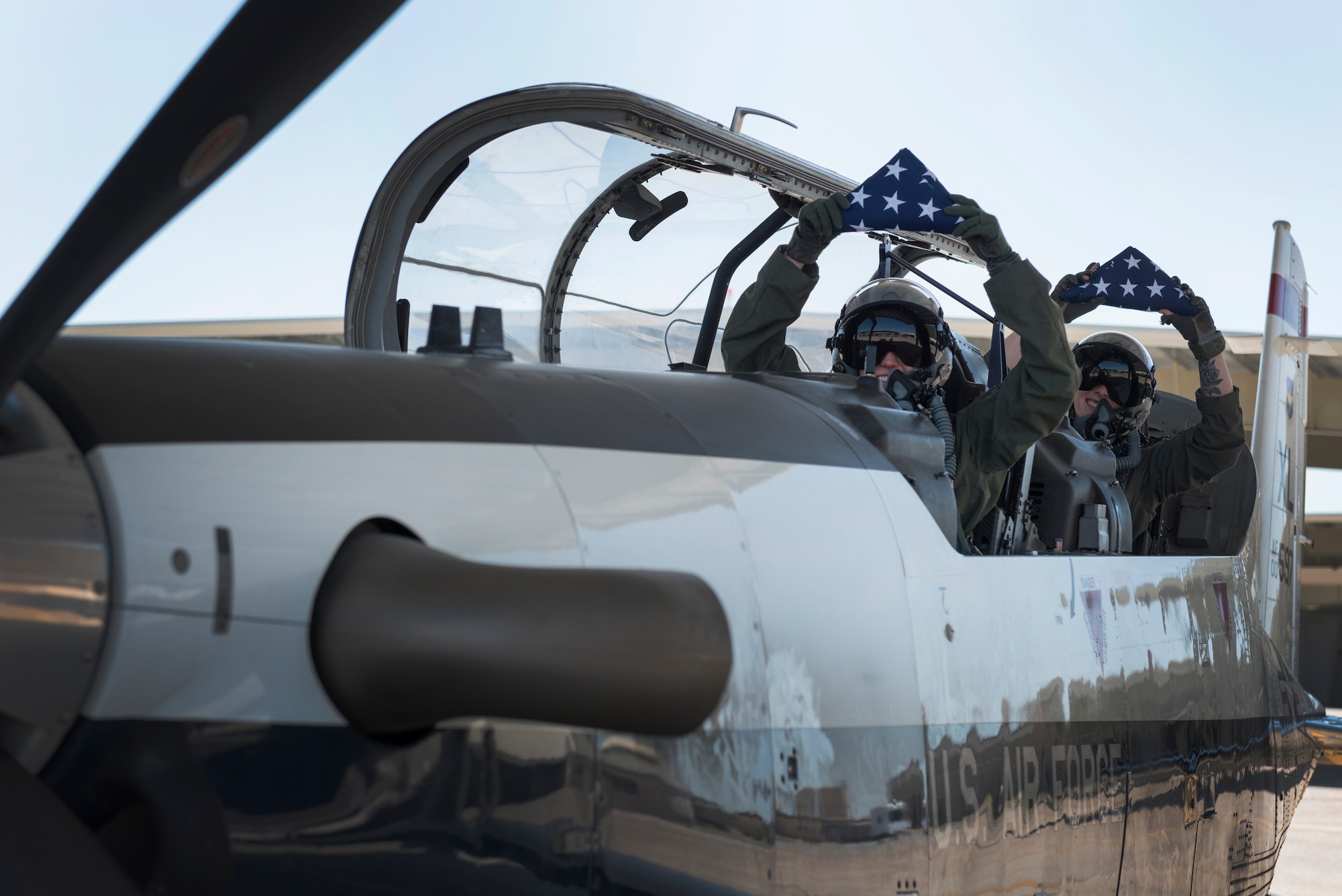 Maj. Camber Governski, 96th Flying Training Squadron T-6A Texan II chief pilot, and 1st Lt. April Wilcox, 85th Flying Training Squadron executive officer, raise the flags they are about to take on their mission of the T-6 she prepares to fly on Aug. 14, 2020 at Laughlin Air Force Base, Texas. The flags they are to fly are for the families of the U.S. Customs and Border Protection service members who were lost to COVID-19. Governski said the experience was a sobering reminder that no one is safe from the virus, and the community must continue to come together and do everything possible to prevent more deaths in the community and globally. (U.S. Air Force photo by Senior Airman Anne McCready)