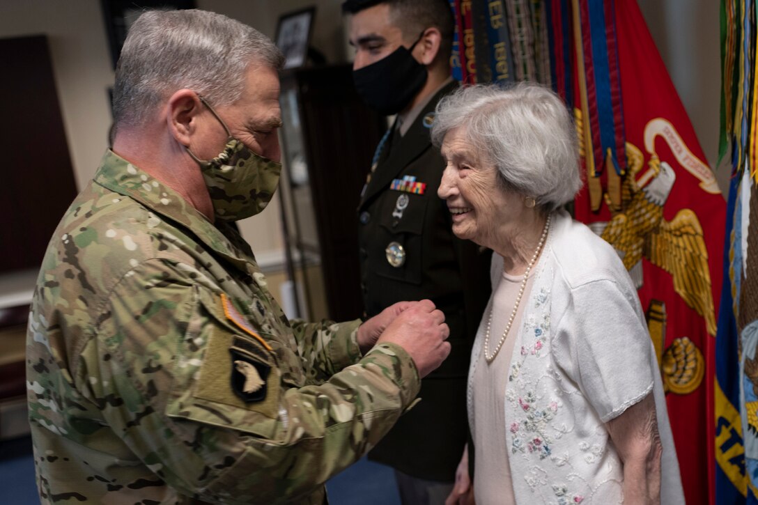A general wearing a face mask presents a medal to a smiling civilian woman.