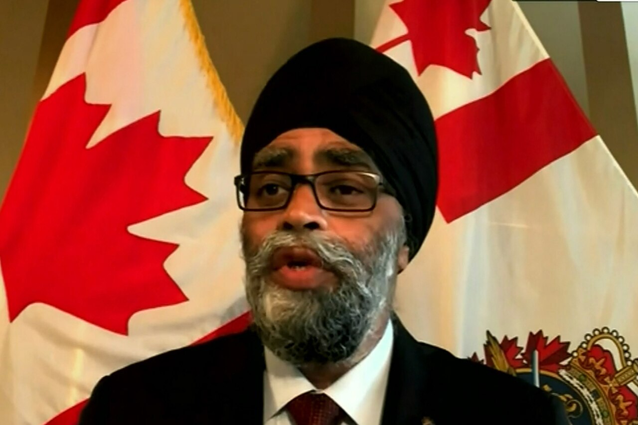 A man standing in front of two Canadian flags is speaking.
