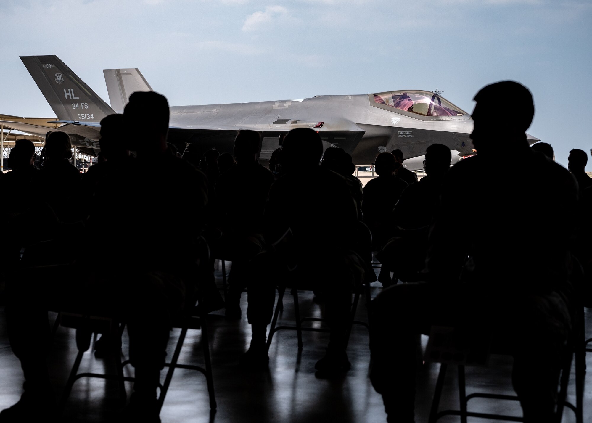 Shadowed personnel sit in front of an F-35A Lightning II at a memorial service.