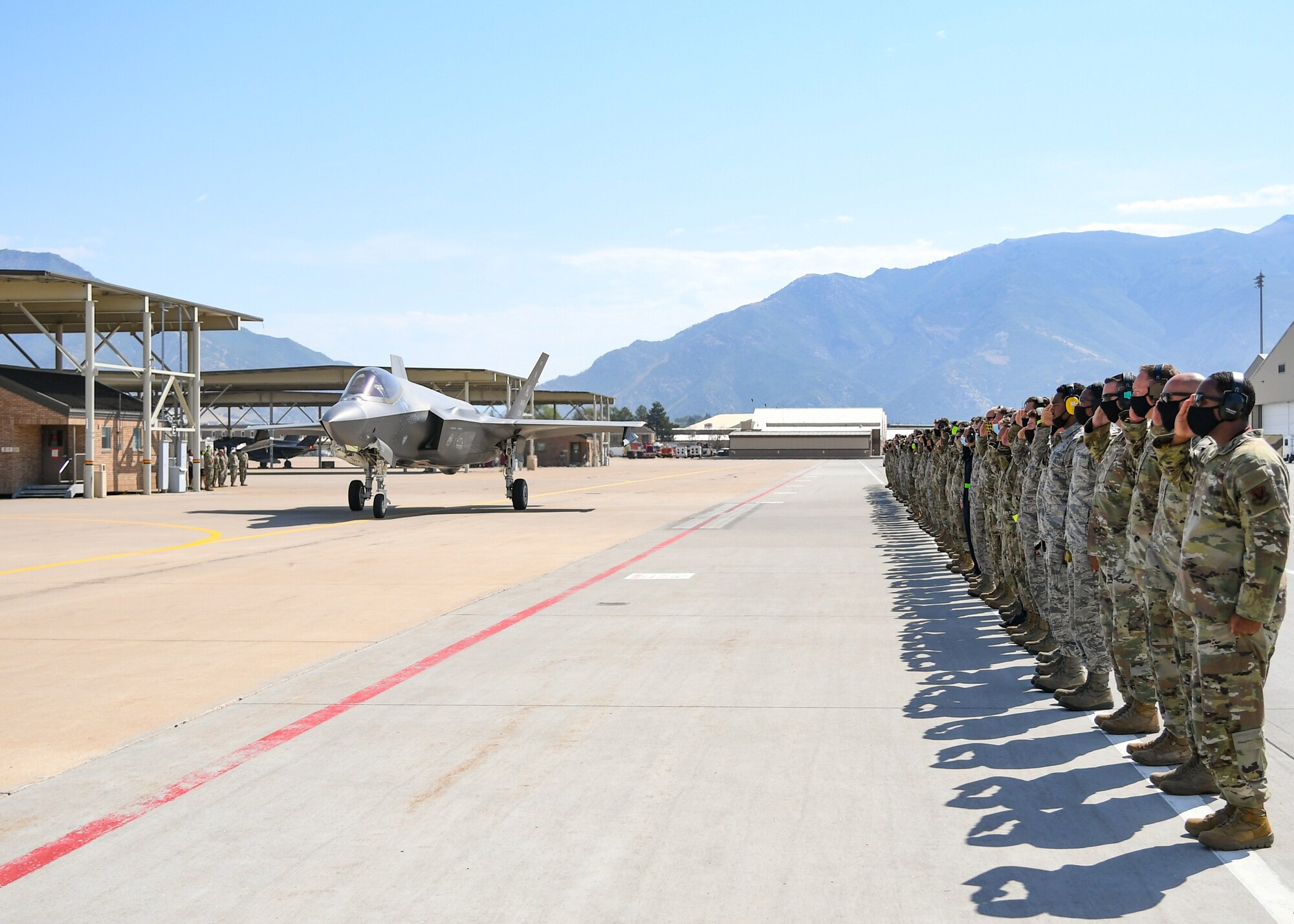 Airman stand on the flightline and salute an F-35