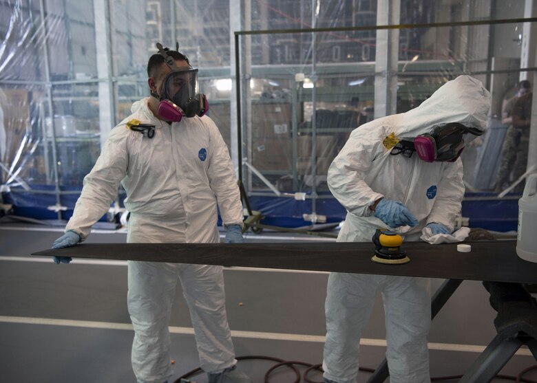 Tech. Sgt. Derek Spencer (left), Aircraft Structural Maintenance Craftsman 374th Maintenance Squadron Fabrication Shop, oversees Airman 1st Class Isaiahlee Elizardo (right), Aircraft Structural Maintenance Journeyman 374th Maintenance Squadron Fabrication Shop, as he prepares to sand a CV-22 blade inside a Retractable Painter Containment System at Yokota Air Base, Japan, August 11, 2020.