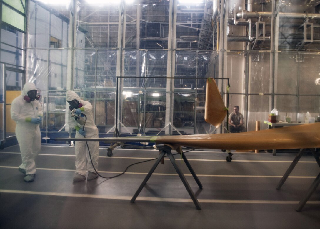 Staff Sgt. Alex Poteet (left), Aircraft Structural Maintenance Craftsman 374th Maintenance Squadron Fabrication Shop, and Airman 1st Class Isaiahlee Elizardo (right), Aircraft Structural Maintenance Journeyman 374th Maintenance Squadron Fabrication Shop, apply a coat of paint primer to a CV-22 blade inside of a Retractable Painter Containment System at Yokota Air Base, Japan, on August 12, 2020.