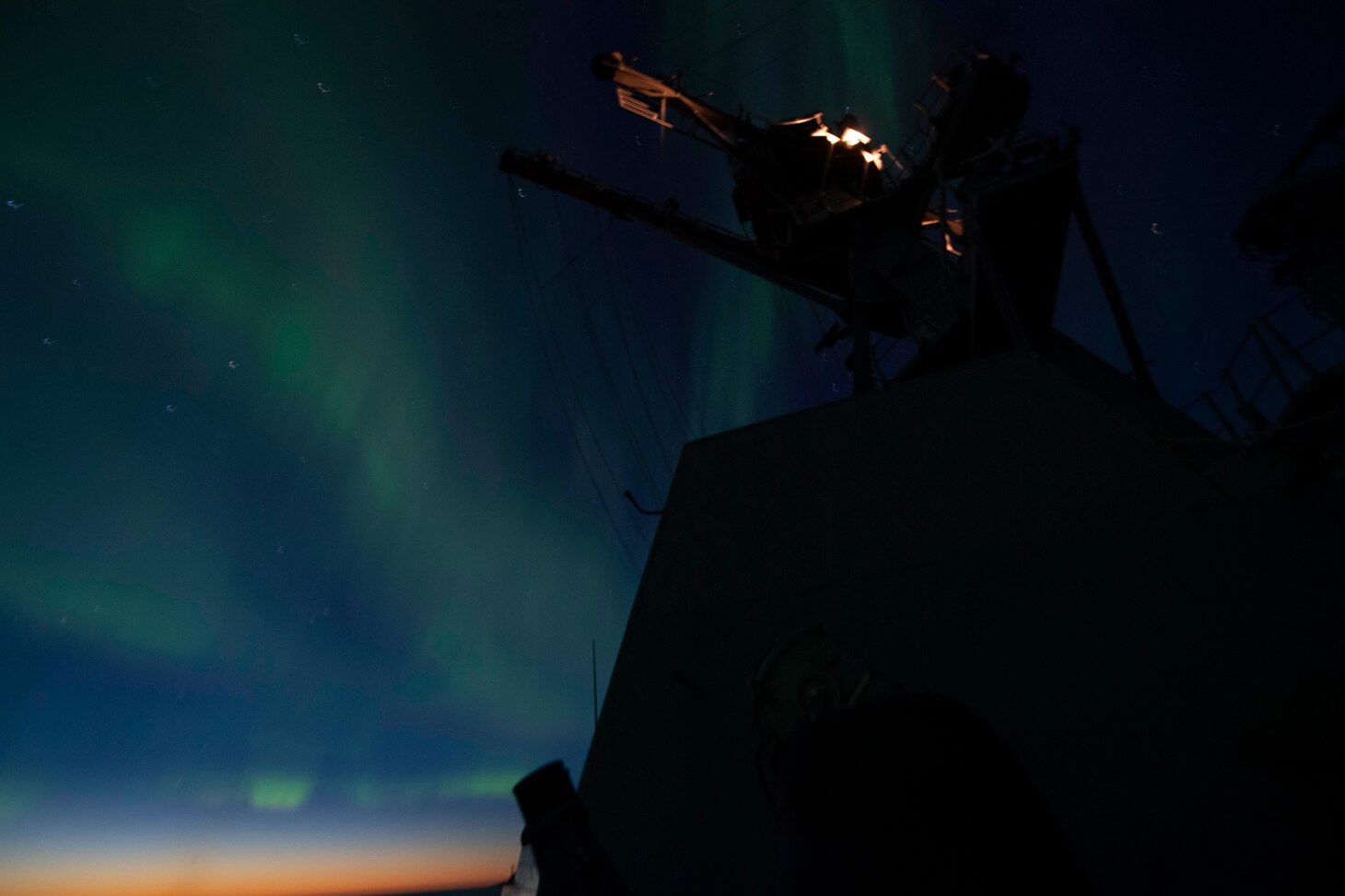 The Aurora Borealis appears in the night sky over the Arleigh Burke-class guided-missile destroyer USS Thomas Hudner (DDG 116).
