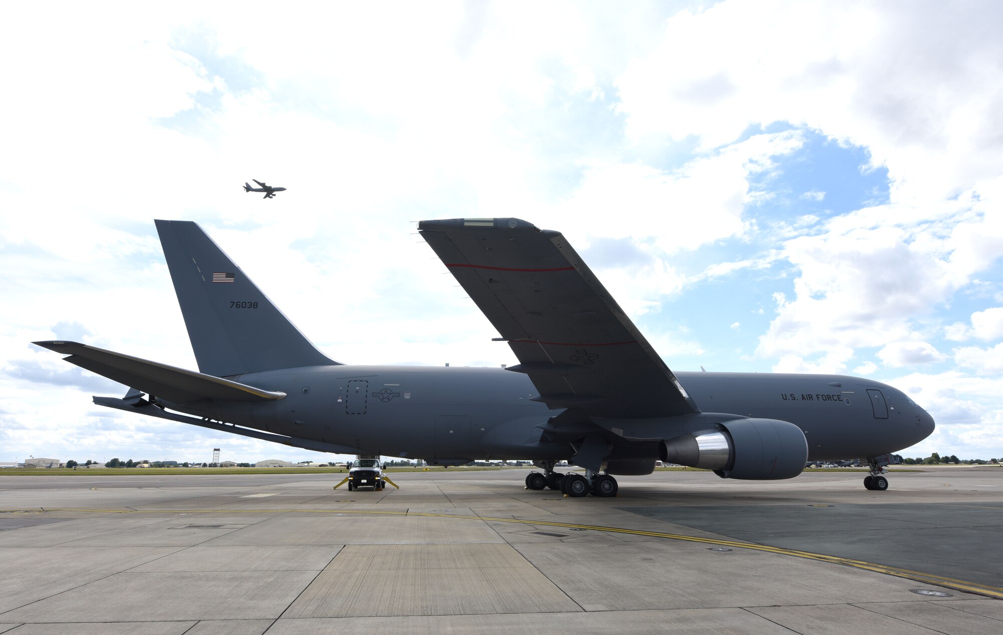 A KC-46A Pegasus sits on the flightline as a KC-135 Stratotanker flies overhead at RAF Mildenhall, England, Aug. 18, 2020. Aircrew and crew chiefs, along with two KC-46s, spent time here to train alongside KC-135 Stratotanker aircrew. (U.S. Air Force photo by Karen Abeyasekere)