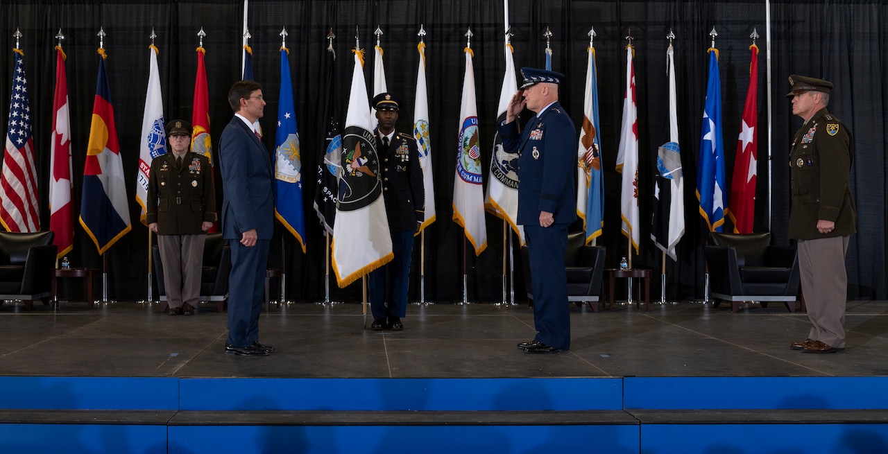 People stand on stage, some in military uniforms, performing a ceremony.