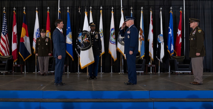 People stand on stage, some in military uniforms, performing a ceremony.