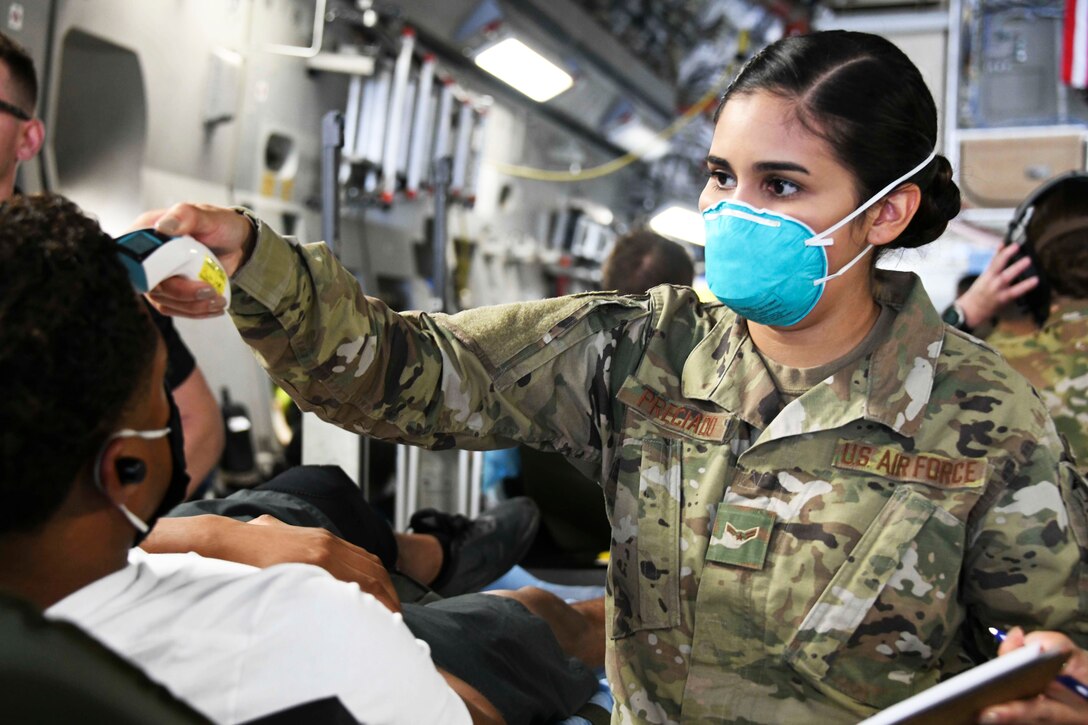 An airman wearing a face mask takes the temperature of a patient.