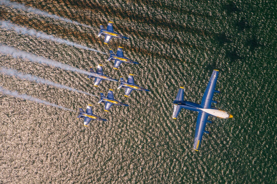 Several aircraft fly in formation over a body of water.