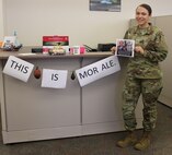 Senior Airman Cindy Delgado, 50th Contracting Squadron contract specialist, stands near and holds ‘The Office’ theme decorations Aug. 21, 2020, at Schriever Air Force Base, Colorado. The base support flight holds weekly morale boosters and Delgado chose ‘The Office’ for her week. (U.S. Air Force photo by Marcus Hill)
