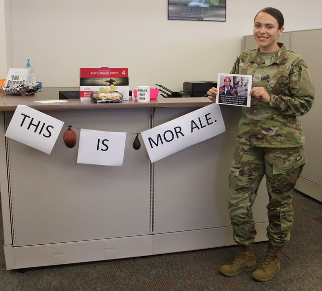 Senior Airman Cindy Delgado, 50th Contracting Squadron contract specialist, stands near and holds ‘The Office’ theme decorations Aug. 21, 2020, at Schriever Air Force Base, Colorado. The base support flight holds weekly morale boosters and Delgado chose ‘The Office’ for her week. (U.S. Air Force photo by Marcus Hill)