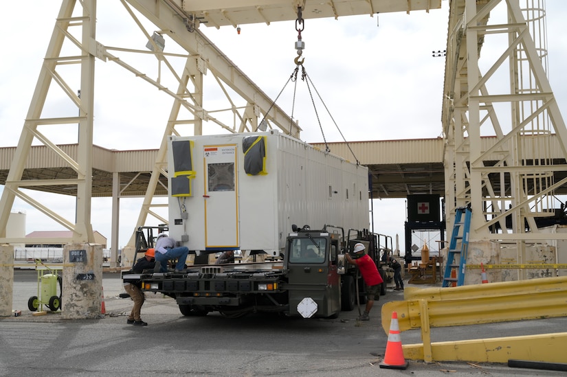 Airmen use a crane to load a negatively pressurized conex onto an awaiting vehicle.