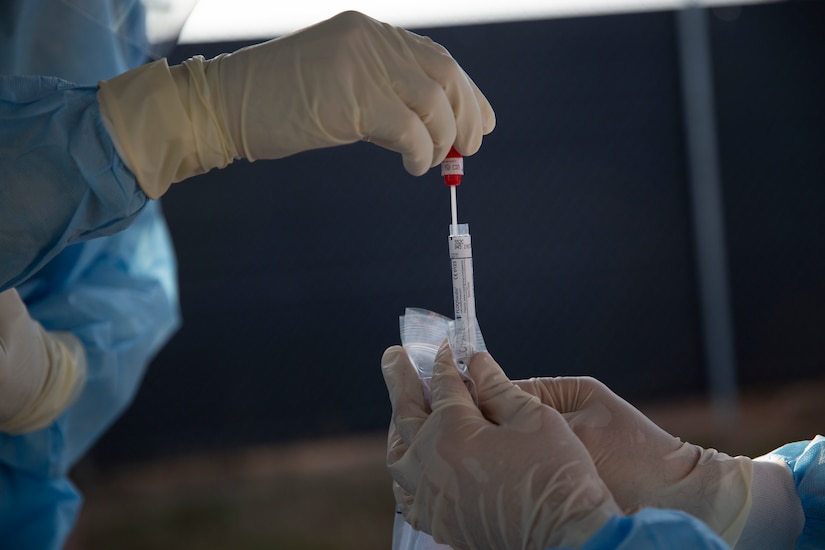 A gloved hand inserts a test swab into a tube.