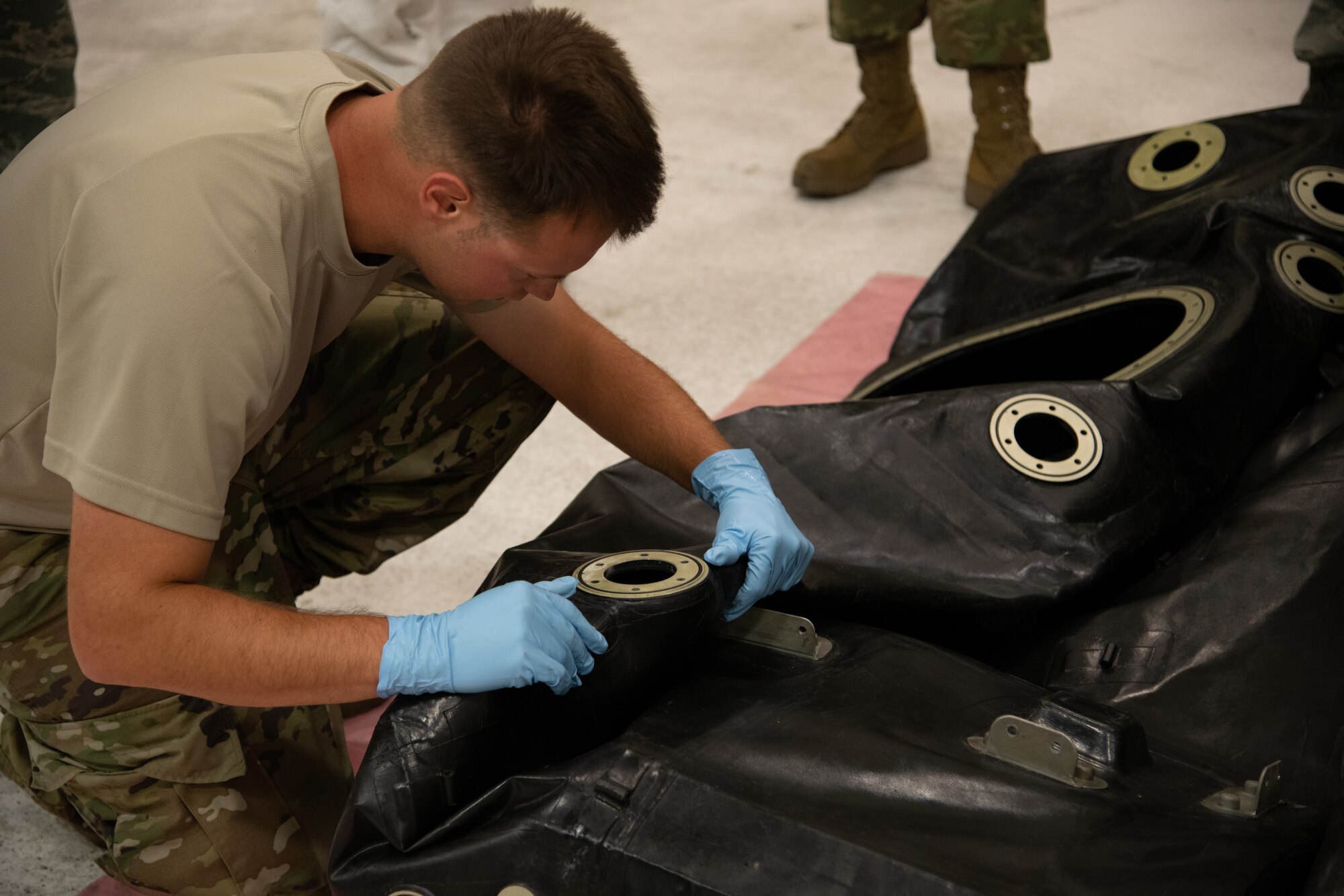 Fuel system technician inspects a metal ring attached to an aircraft auxiliary fuel cell.