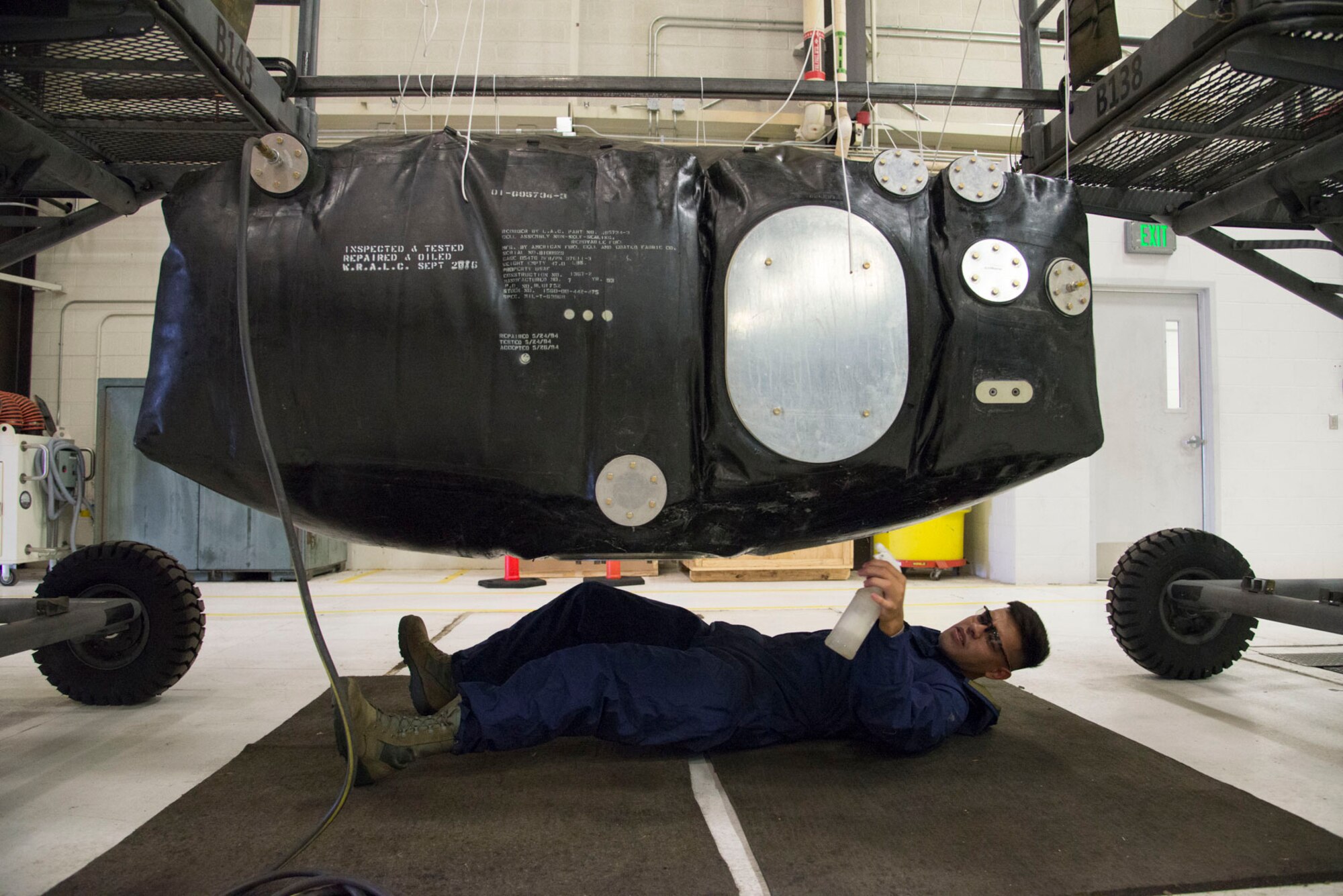 Fuel system technician laying on the ground spraying soapy water from a spray onto an inflated aircraft fuel cell.