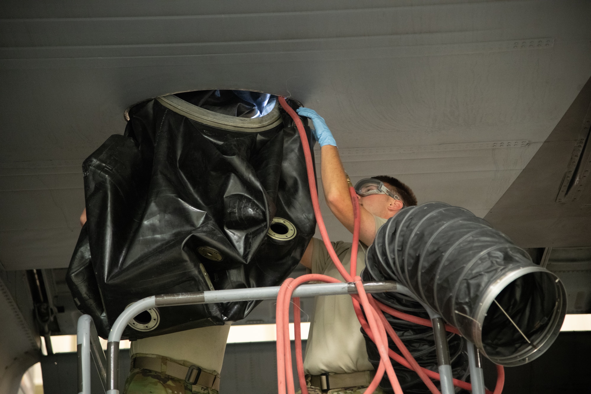 Fuel system technicians pull a fuel cell out from a door on the underside of a C-130 aircraft wing.