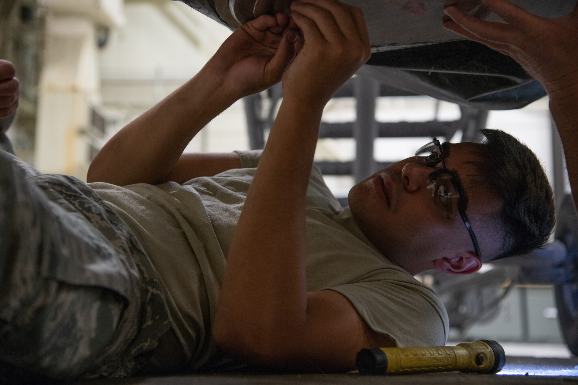 Fuel cell technician laying on the ground inserts screws into a plate that fits onto an aircraft fuel cell.