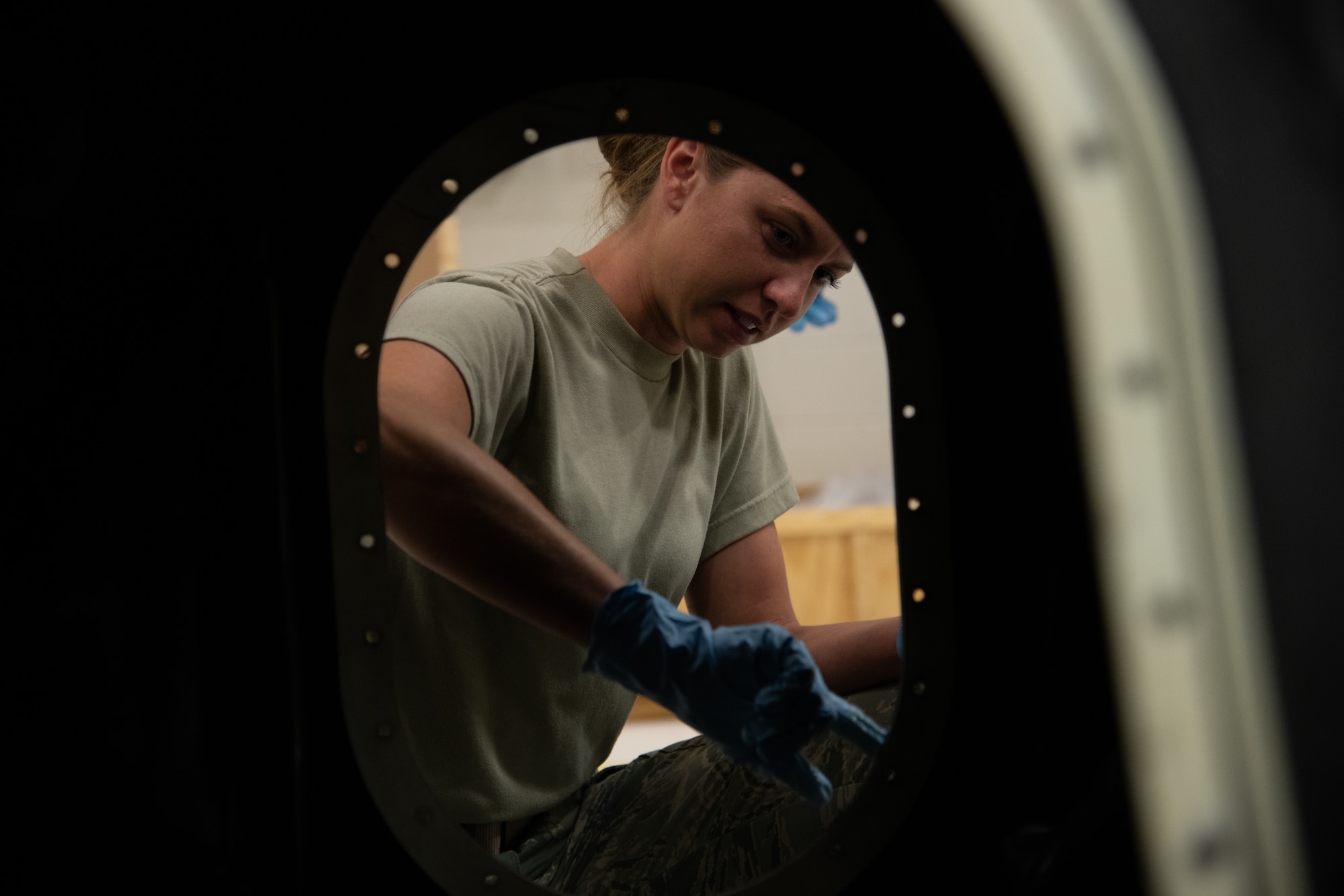 Fuel technician applies grease to metal frame of an aircraft fuel cell.