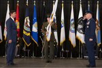 Three men stand on stage with the one in the middle holding a flag.