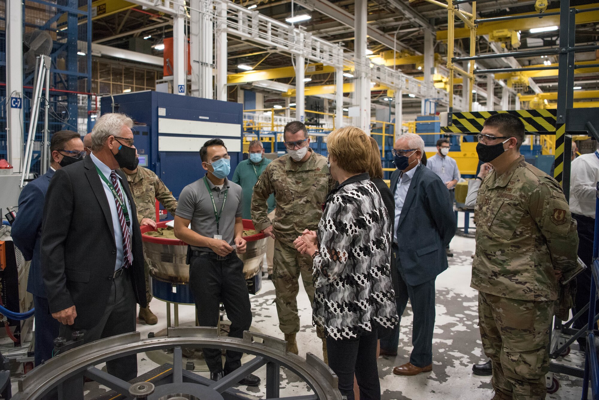 Group of Airmen and Civilians talking inside jet engine repair area.