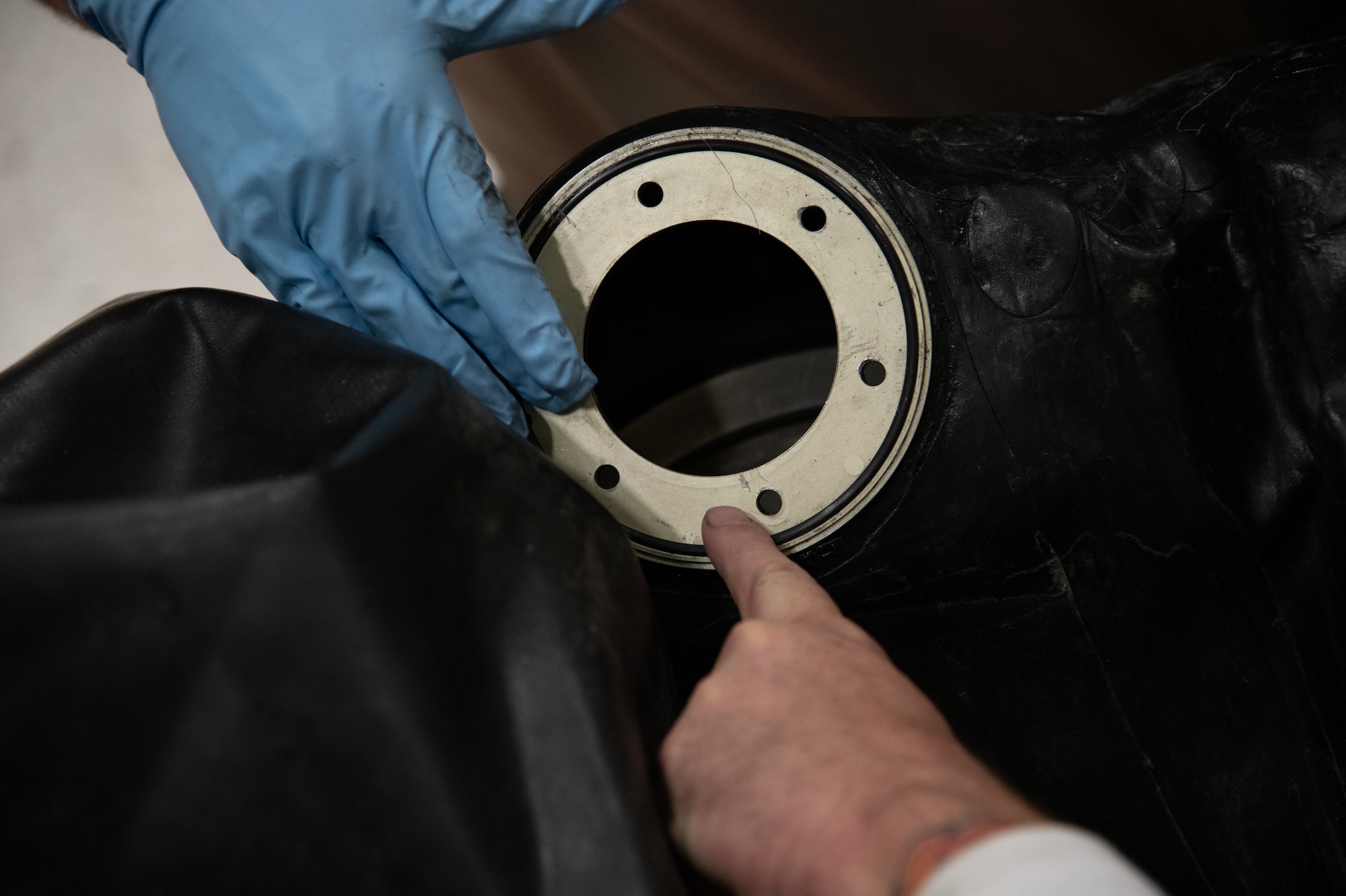 Two hands point at a damaged metal ring on an aircraft auxiliary fuel cell.