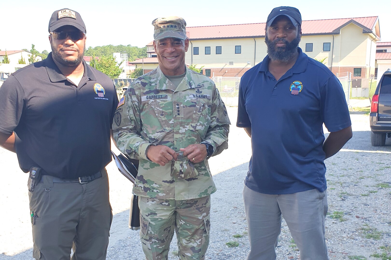 Two civilian men in blue polos stand next to a military man for a photo op