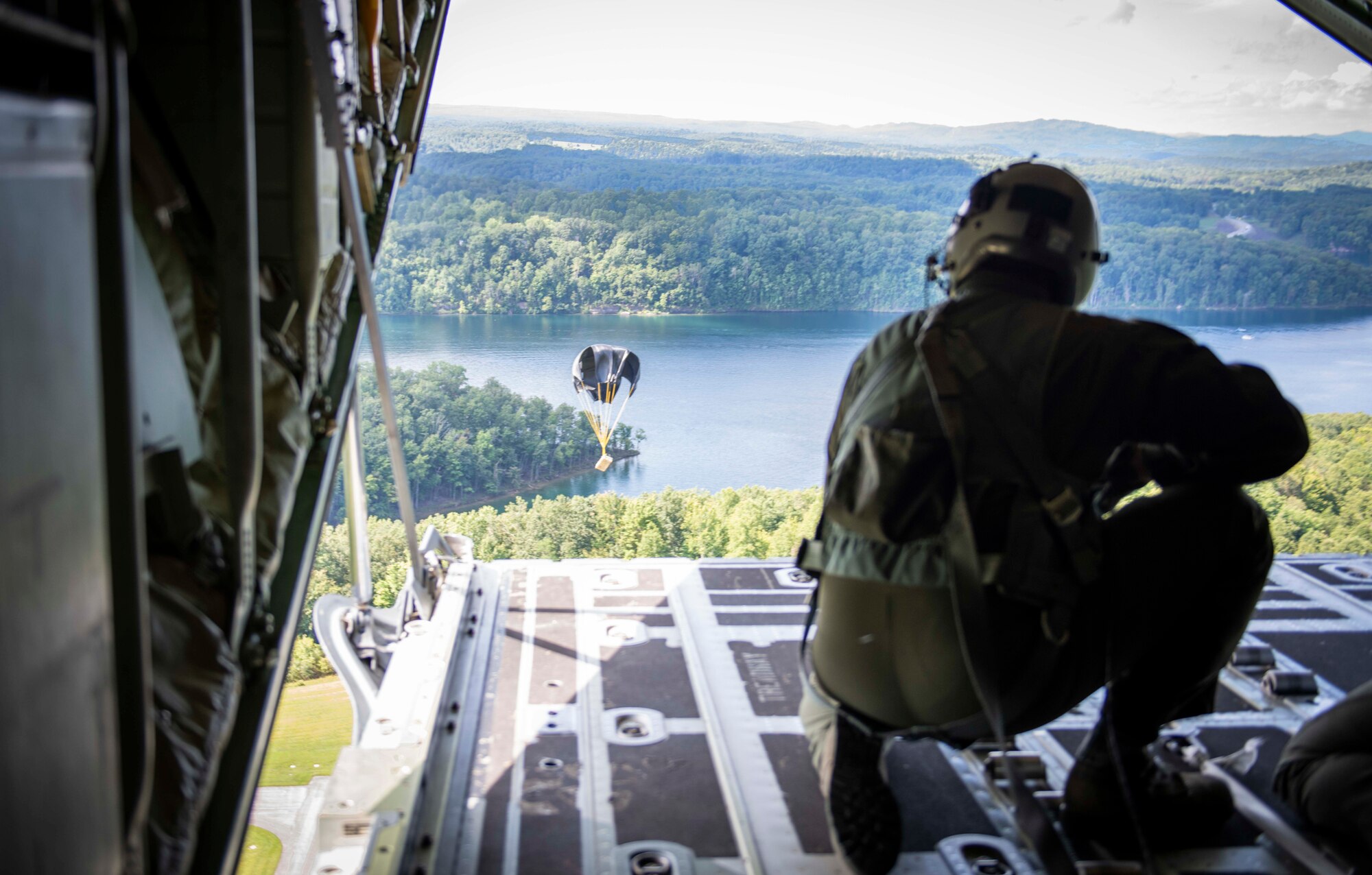 Air Force Reserve loadmaster watches cargo descend toward a drop zone after it is pushed out of the back of a C-130J Super Hercules near Charleston, W. Va., Aug. 23, 2020. Eight C-130s and Reserve and Guard partners converge to participate in a week-long training event. The exercise was designed to test the abilities of Air Force Reserve units to execute rapid global mobility missions in challenging, contested scenarios. (U.S. Air Force Reserve photo by Senior Airman Nathan Byrnes)