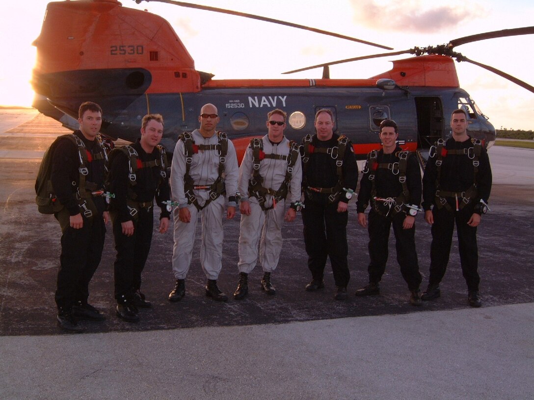 Pararescue Jumpers in Jump gear stand in front of an orange helicopter in Guam.