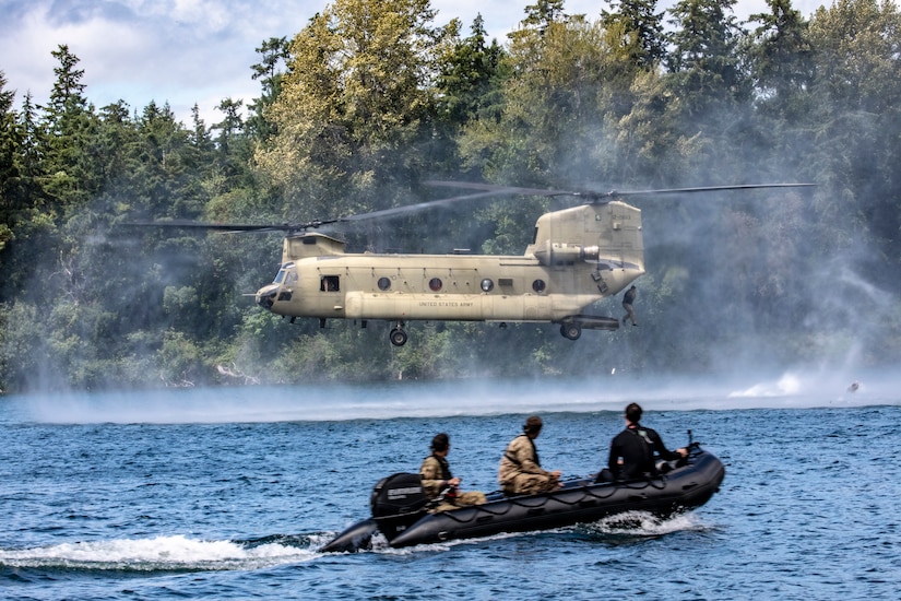 A soldier jumps into a lake from a helicopter while other troops in a rubber boat move through the water.