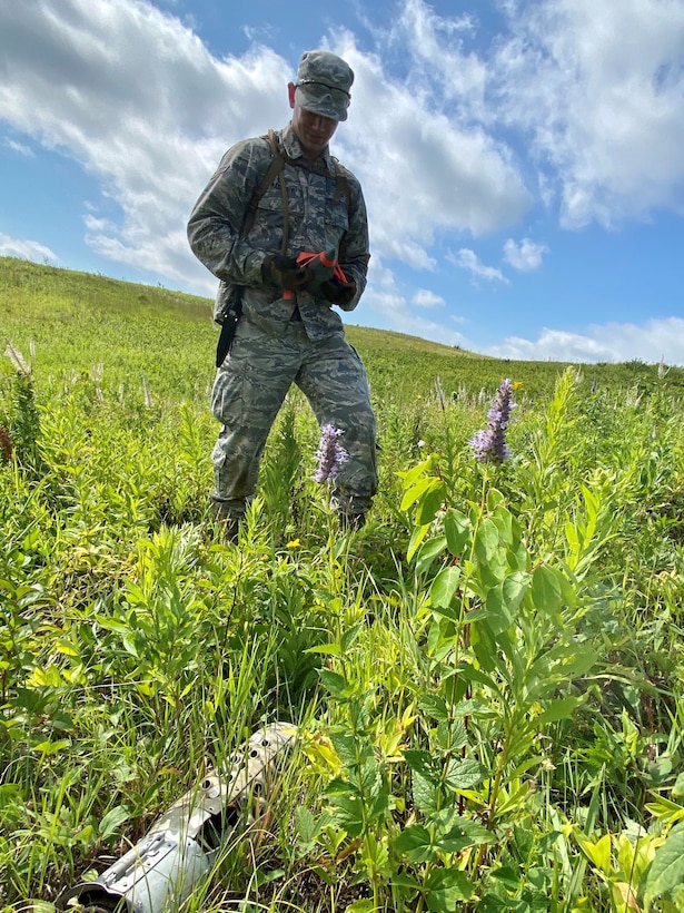 An airman walks in a field with explosive equipment ahead of him.