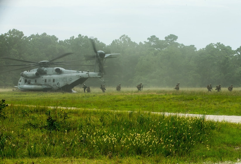Marines exit a helicopter in a lush green field.