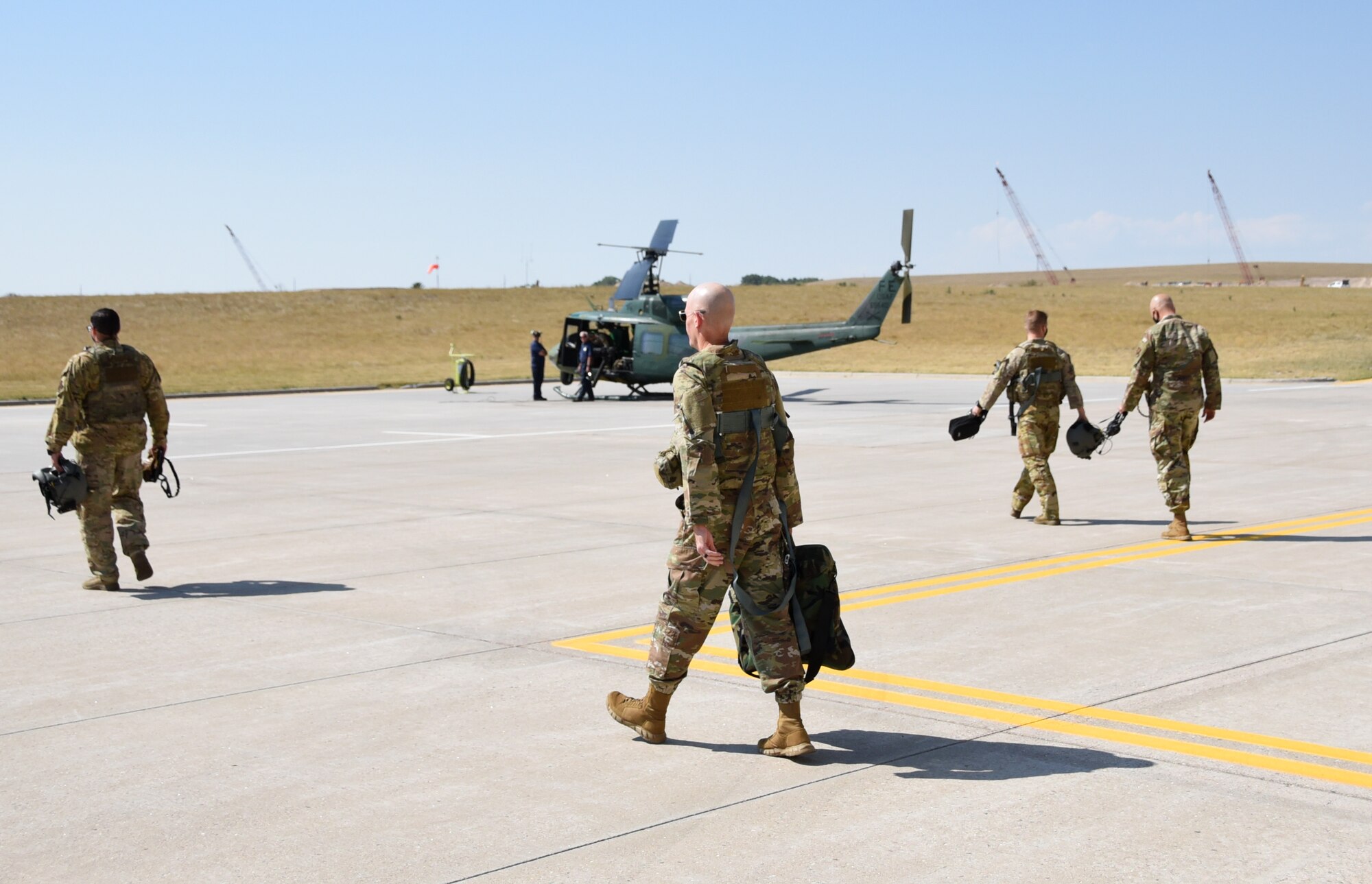 Airmen walk on runway toward UH-1N helicopter.
