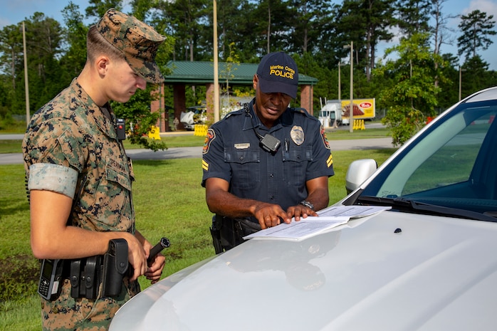 U.S. Marine Corps Lance Cpl. Samuel Spearman, left, military police officer, gets instruction from McGill Howard, right, civilian police officer, as part of the Field Training Officer program at the main gate on Marine Corps Air Station New River, North Carolina July 31, 2020. MCAS New River has introduced the Field Training Officer program in order to ensure that military police officers are trained to be more proficient and skillful at their duties. Both Howard and Spearman are police officers with Headquarters and Support Battalion, Marine Corps Installations East-Marine Corps Base Camp Lejeune. (U.S. Marine Corps Photo by Lance Cpl. Isaiah Gomez)