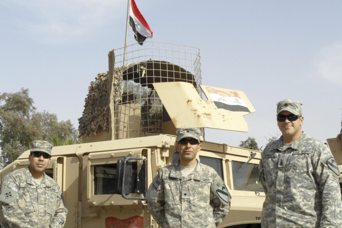 Three soldiers stand in front of a military vehicle.