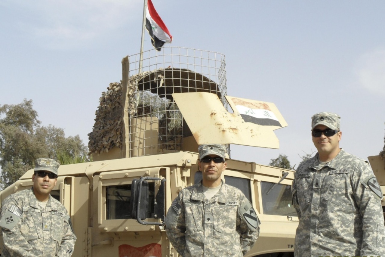 Three soldiers stand in front of a military vehicle.