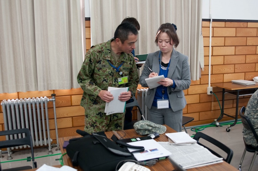 An interpreter goes over notes with a man in a military uniform.