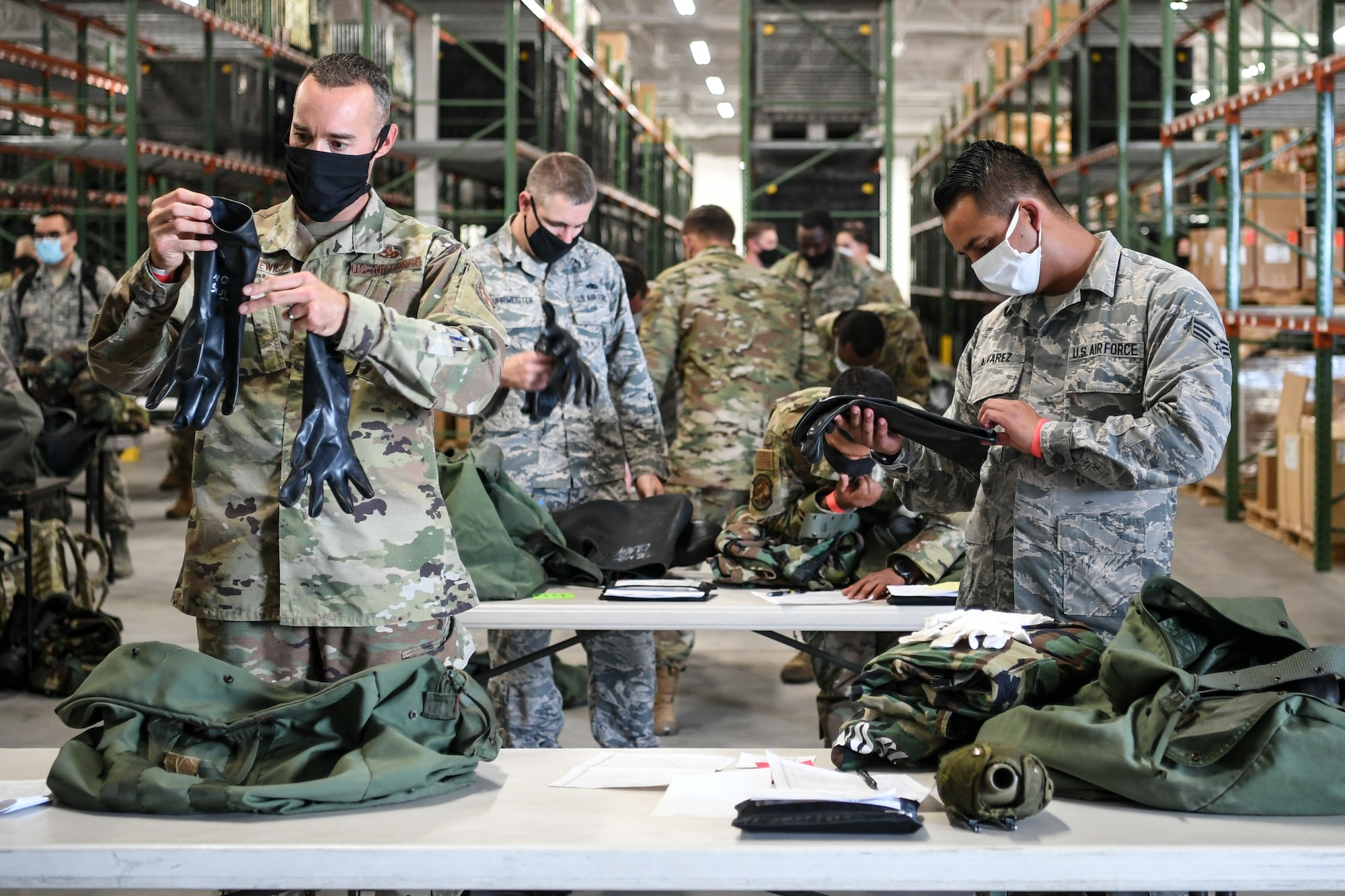 Dozens of Airmen check their deployment gear on tables.