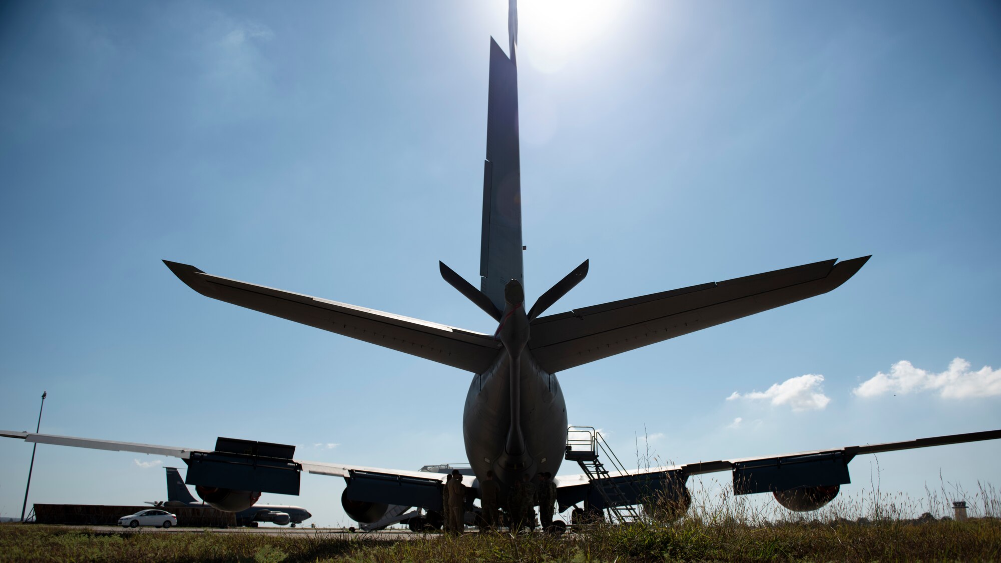 A KC-135 shown from behind on a bright sunny day, eight Airmen stand under the tail of the plane talking about the boom-pod mid-air refueling equipment August 17, 2020.