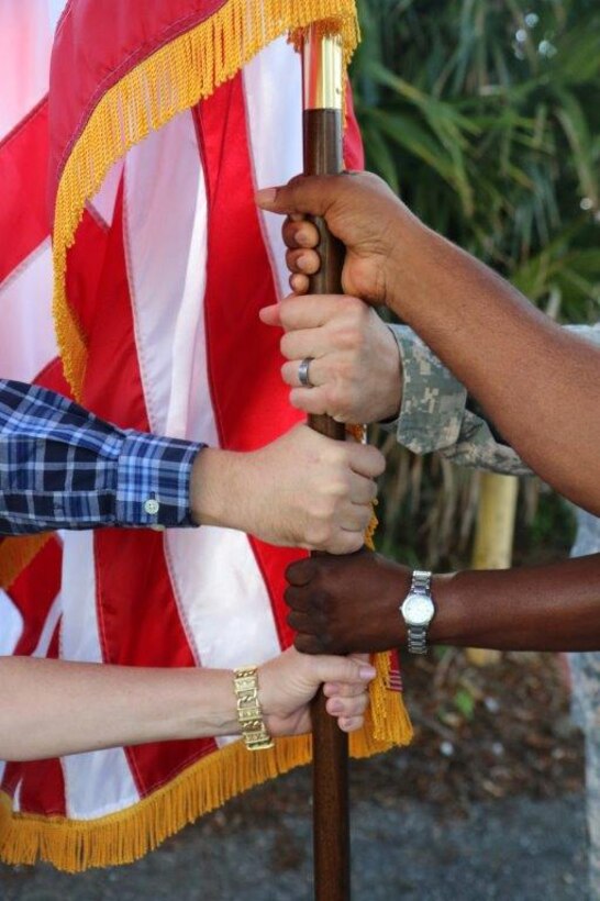 Five people with different ethnicities hold on the American flag.