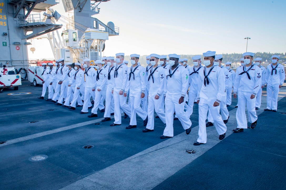 A group of sailors wearing face masks walk in formation.
